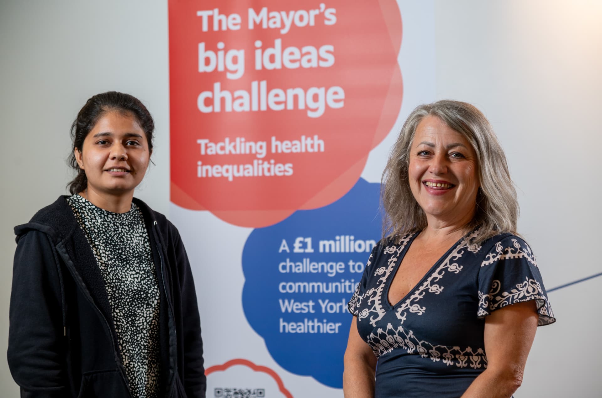Two members of the UKind team in front of a Mayor's Big Ideas Challenge banner