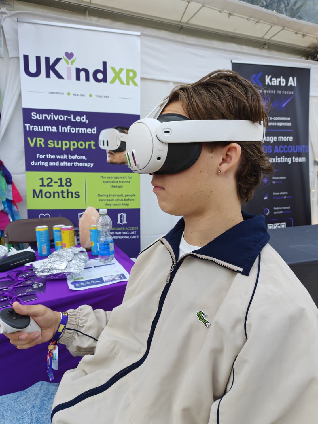 A participant using a UKind XR headset and controller in front of the UKind XR banner